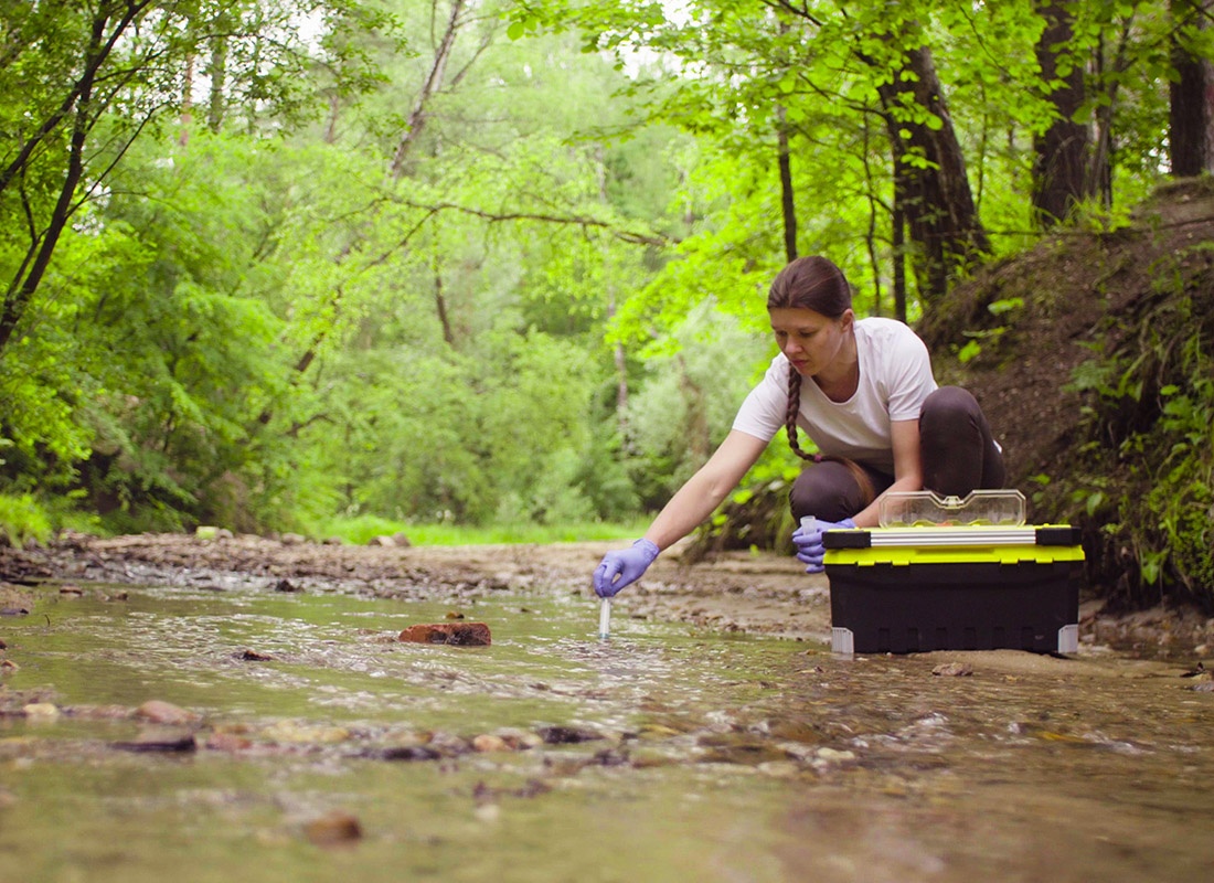 About Our Agency - Environmental Scientist Sitting Near the Creek Taking a Sample of Water