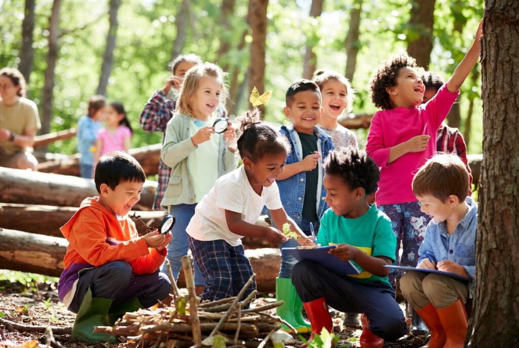 Diverse group of children learning outdoors in forest school program covered by Conservation United insurance